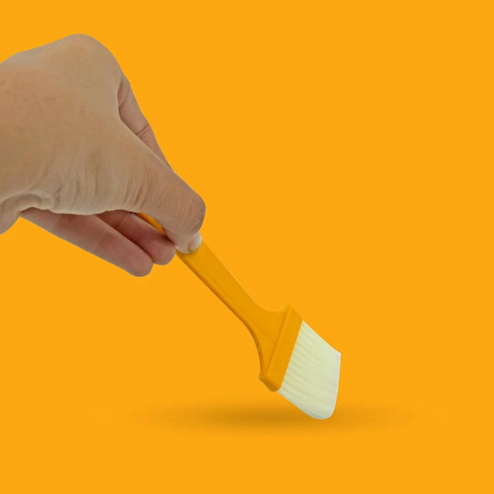 Hand holding a yellow silicone multifunction basting brush set for cooking and grilling
