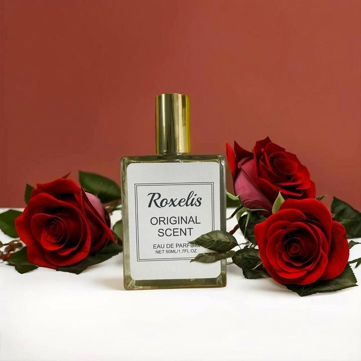 Roxelis Original Scent perfume bottle with gold cap surrounded by red roses on white surface