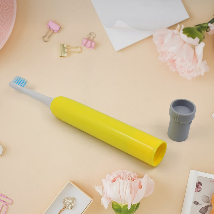 Bright yellow waterproof electric toothbrush on a pastel background with flowers and stationery