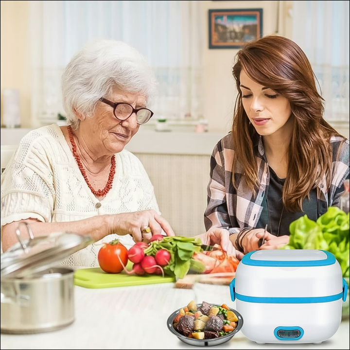 White and blue 2-tier portable electric lunch box with metal food tray and vegetables, shown in a kitchen.