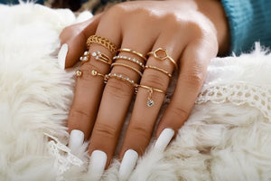 Hand wearing multiple gold rings on a fluffy white surface