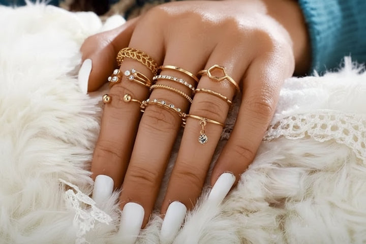 Hand wearing multiple gold rings on a fluffy white surface
