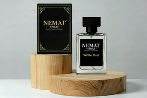 Nemat White Oud spray perfume bottle and black box on wooden pedestals. Clear glass bottle with black square cap.