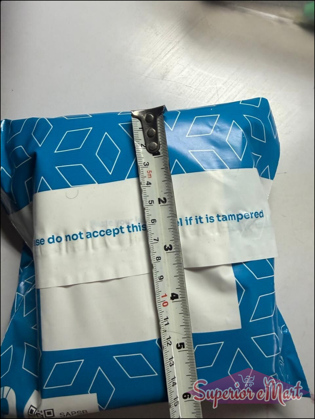 Blue diamond-patterned mailer measured at 6 inches with a tape measure. Label: Please do not accept if tampered.