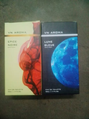 Two VN Aroma perfume boxes placed side by side on a dark gray surface. The left box is labeled EPICE NOIRE with a cream background and red abstract artwork.