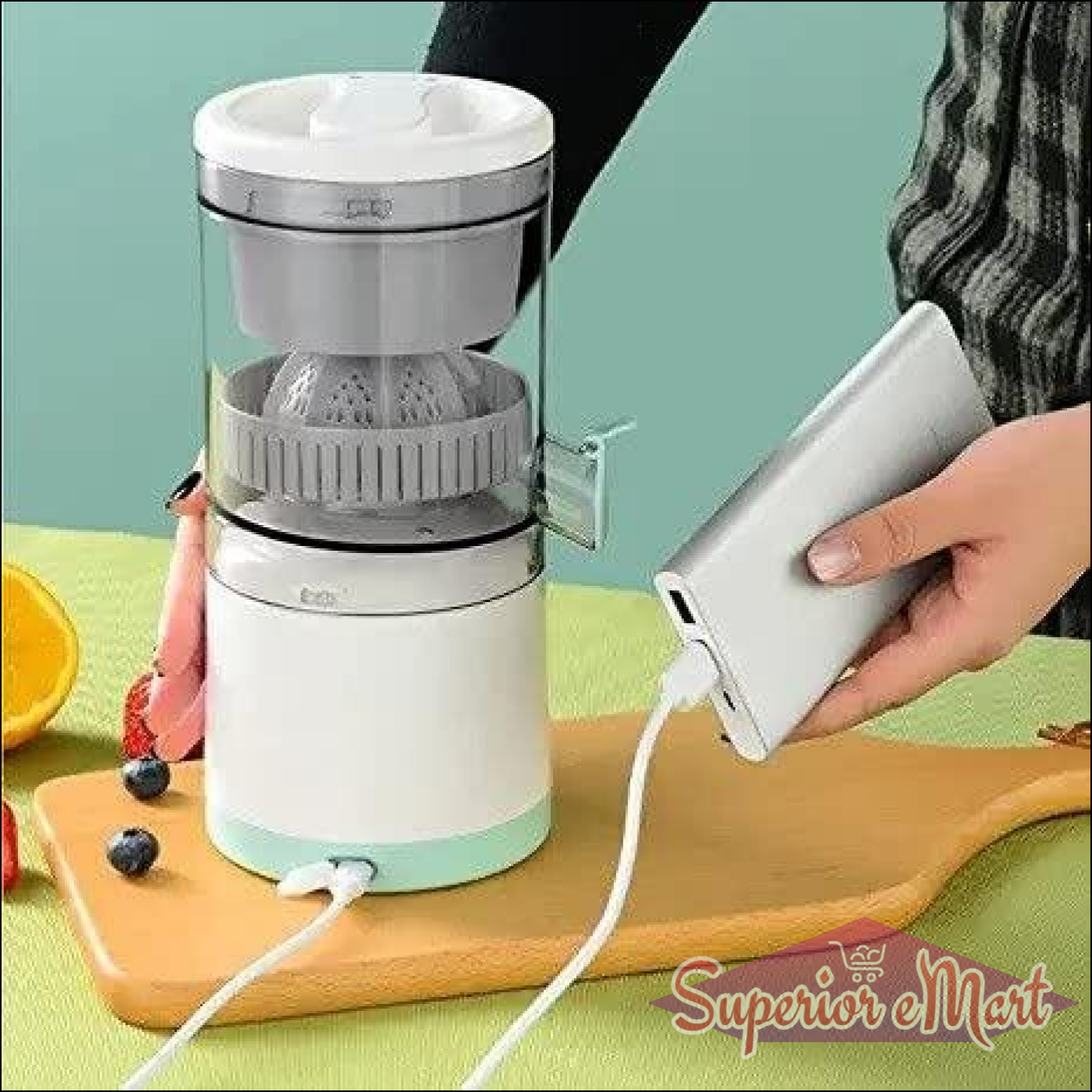 White portable citrus juicer with clear top, charging via USB from a silver power bank on a wooden board.