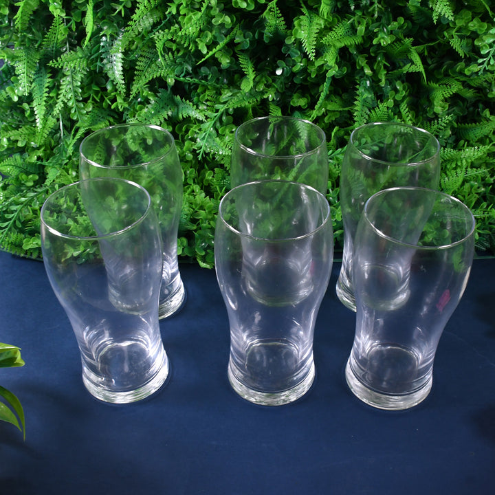 6-piece glass tumbler set arranged on a table with green foliage in the background