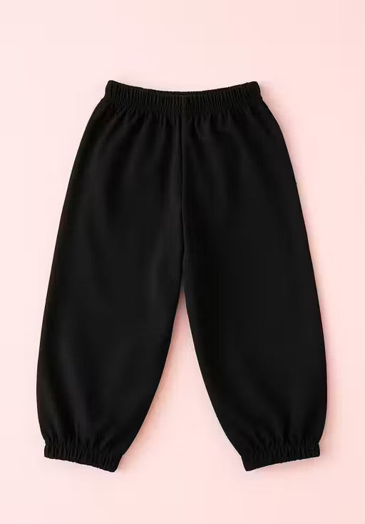 Black elastic-waist and elastic-calf pants laid flat on a light pink background.