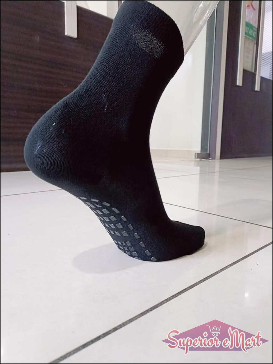 Black knit crew sock with non-slip grey grips on the sole, shown on a mannequin foot.