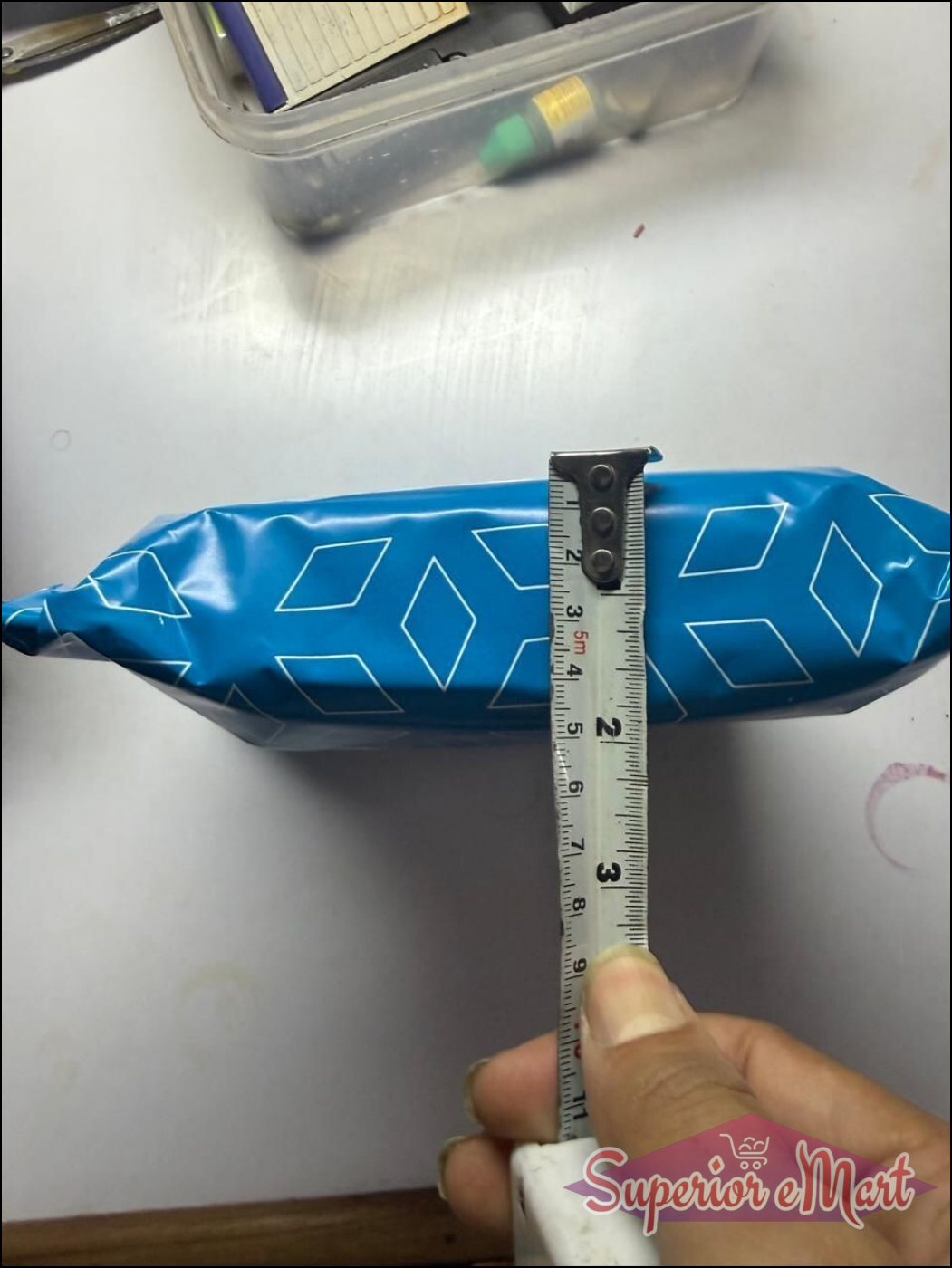 Blue plastic package with white diamond patterns being measured with a tape measure, showing a width of about 5 cm.