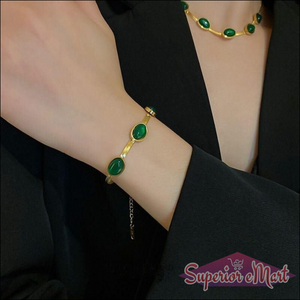 Gold-toned bracelet and necklace featuring oval green stones, worn by a person in a black blazer.