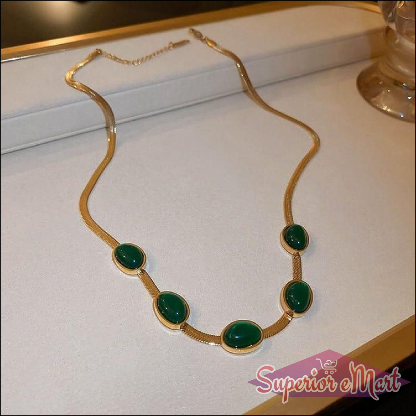 Gold herringbone chain necklace with five oval green stones in polished bezel settings.