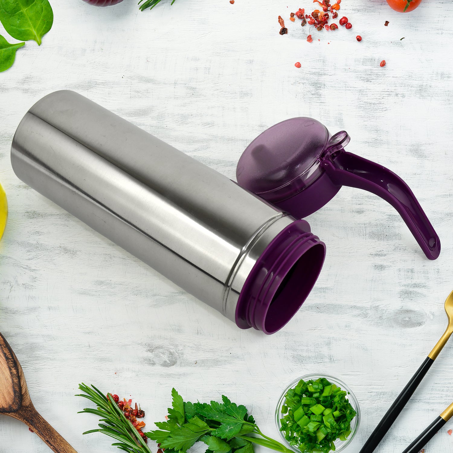 Stainless steel oil pourer with purple lid and handle placed on kitchen counter with herbs and spices