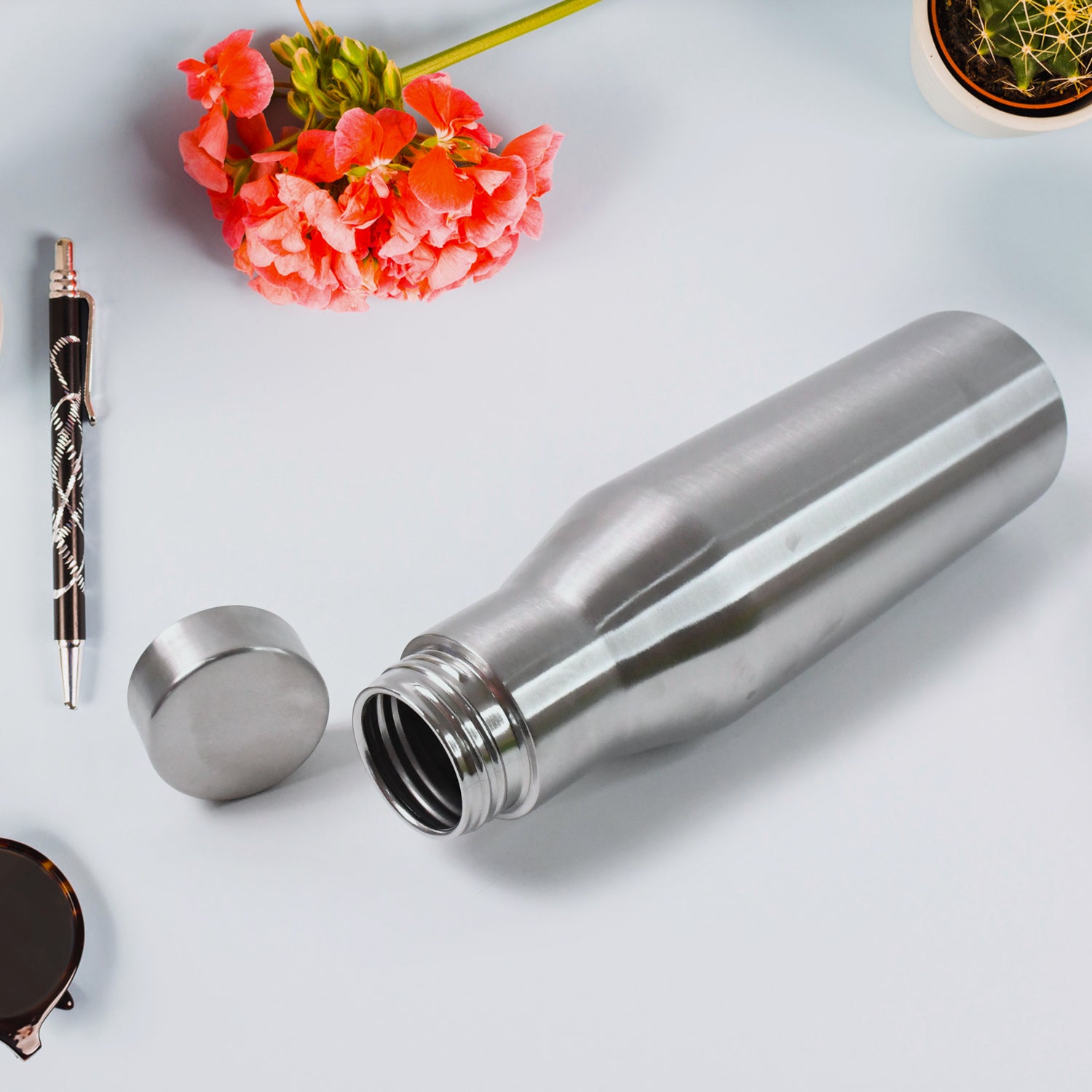 Superior eMart stainless steel insulated water bottle open with cap beside pink flowers on white surface