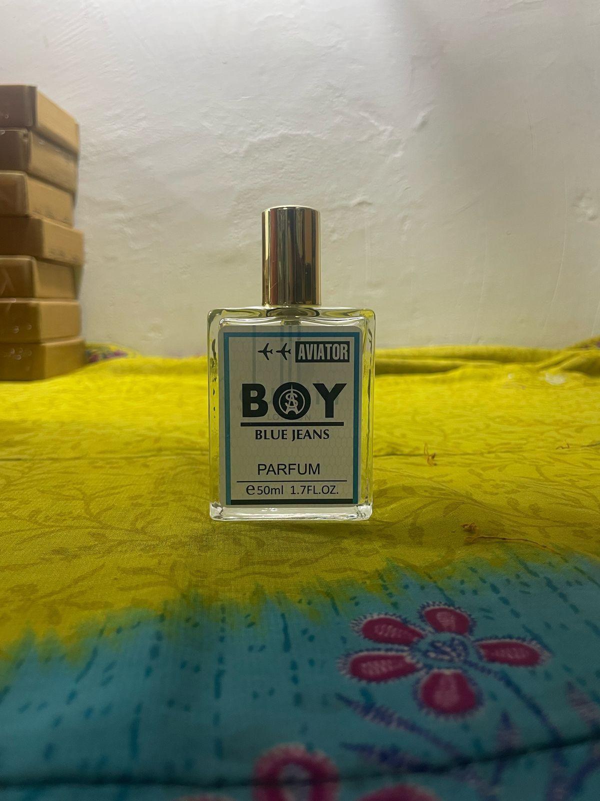 Aviator Boy Blue Jeans fragrance 50ml in clear bottle with gold cap on colorful fabric background