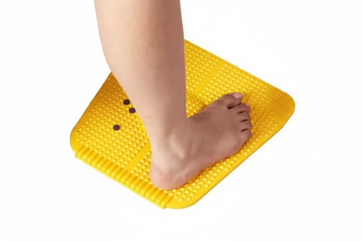 A close-up of a person's foot and lower leg stepping onto a bright yellow textured floor pad with raised nubs, shown against a plain white background.