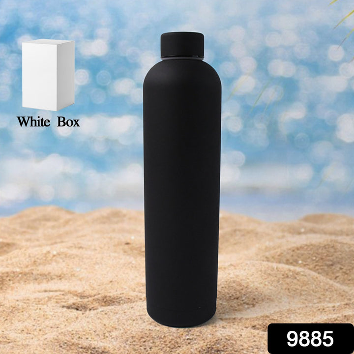 Black double wall water bottle 1000ml standing on sandy beach with a white box shown