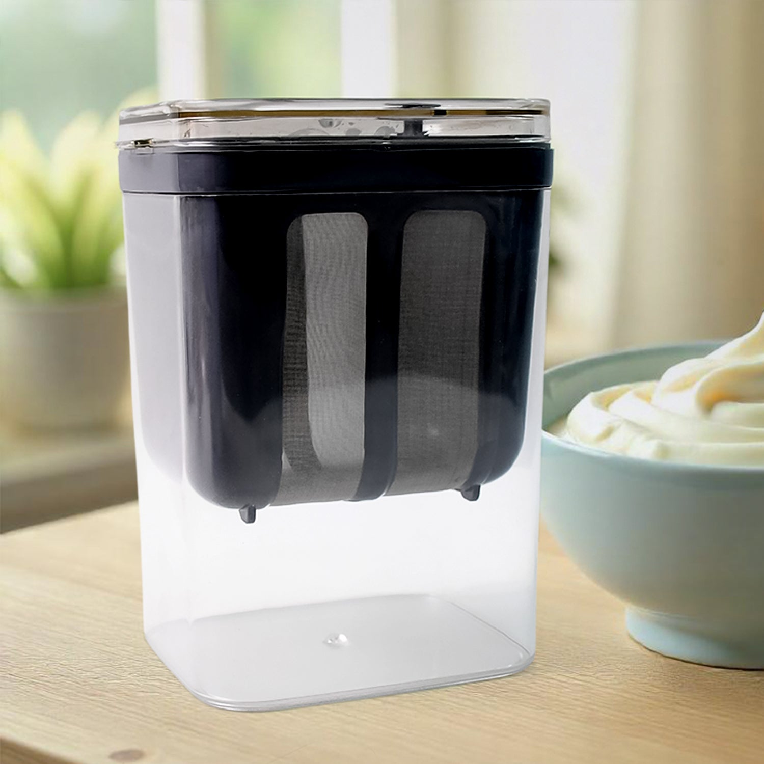 Superior eMart yogurt strainer with storage in clear container on wooden table next to a bowl of creamy yogurt
