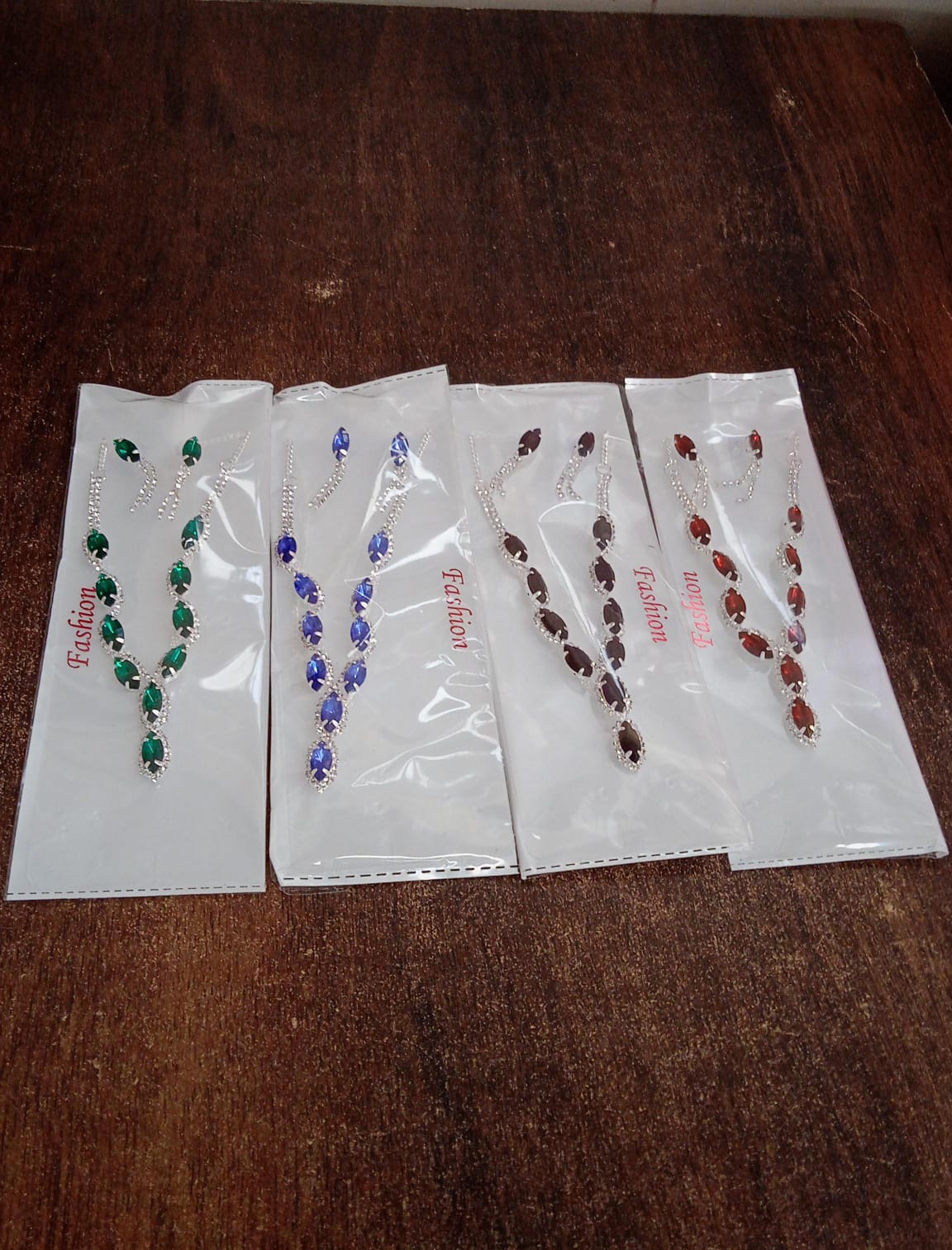 Set of four elegant bridal necklace and earrings in various colors displayed in protective packaging