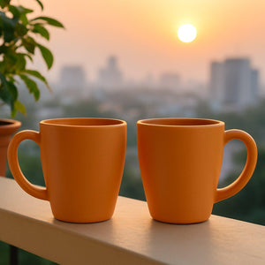 Ceramic coffee and tea mugs set in vibrant orange color against a sunset backdrop