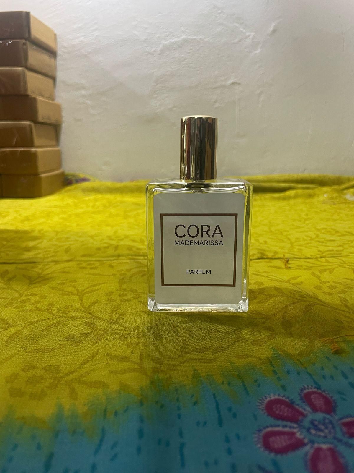 Cora Mademarissa perfume 50ml bottle with gold cap on yellow and blue fabric background