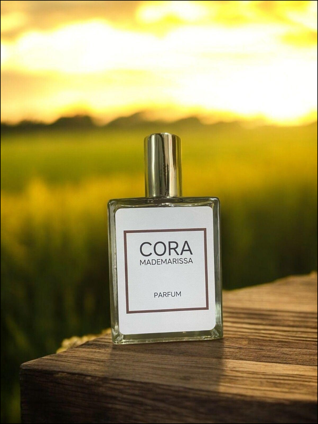 Cora Mademarissa perfume 50ml bottle on a wooden surface with a sunset background