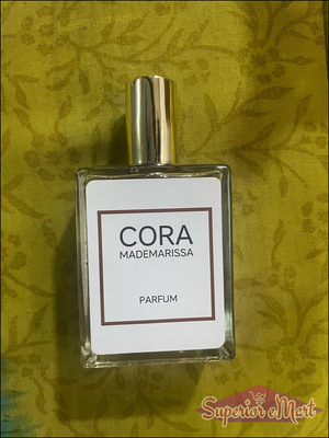 Cora Mademarissa perfume 50ml in a clear glass bottle with a gold cap on a textured green background