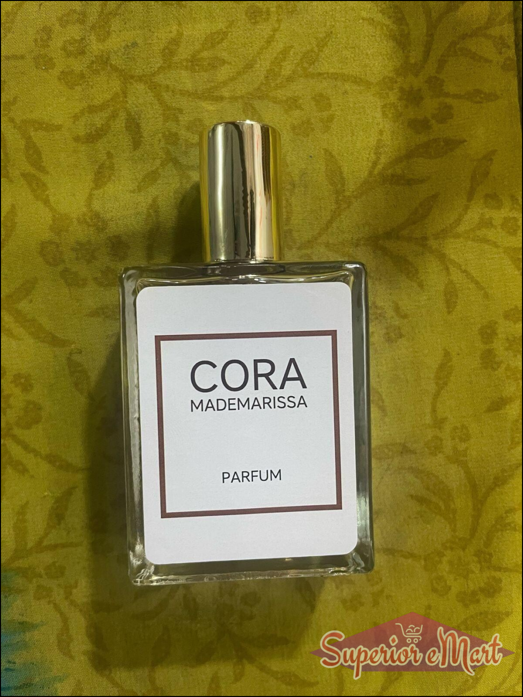 Cora Mademarissa perfume 50ml in a clear glass bottle with a gold cap on a textured green background