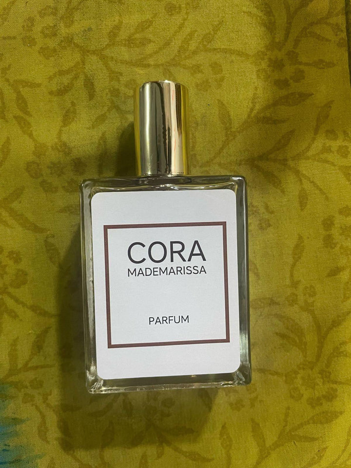 Cora Mademarissa perfume 50ml in a clear glass bottle with a gold cap on a textured green background