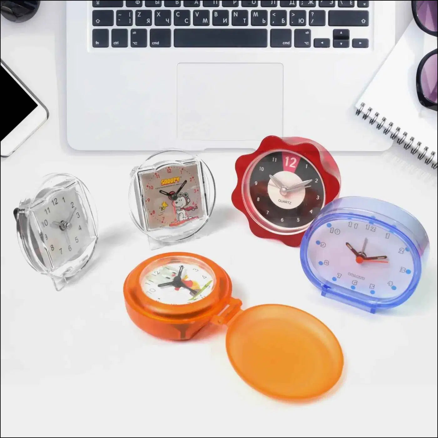 Colorful decorative clocks for every room displayed on a desk with a laptop and accessories