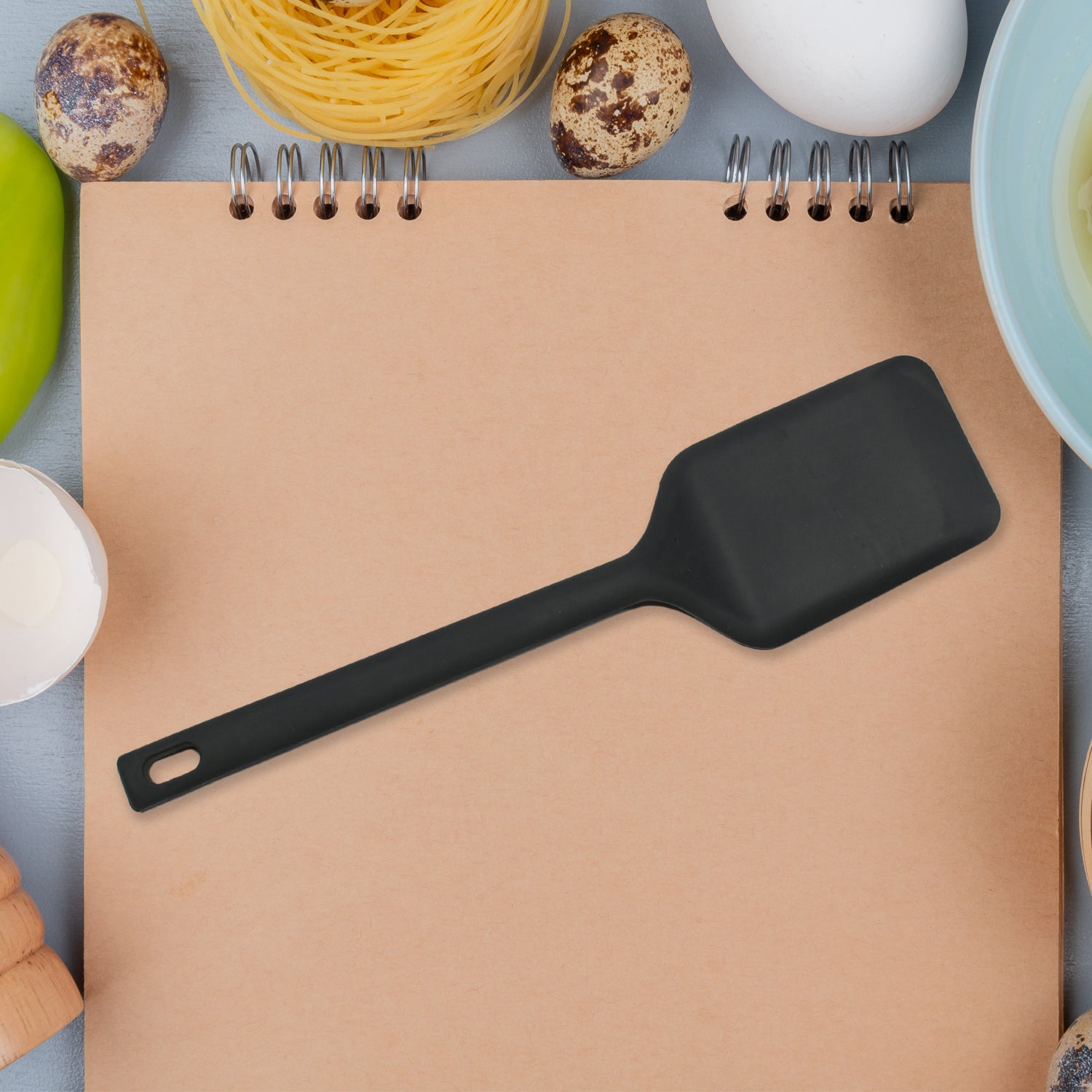 Black silicone dessert serving spatulas on a kitchen notepad surrounded by cooking ingredients