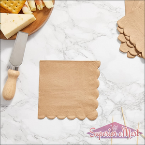 Scalloped edge disposable napkins in tan color on a marble table with a cheese platter