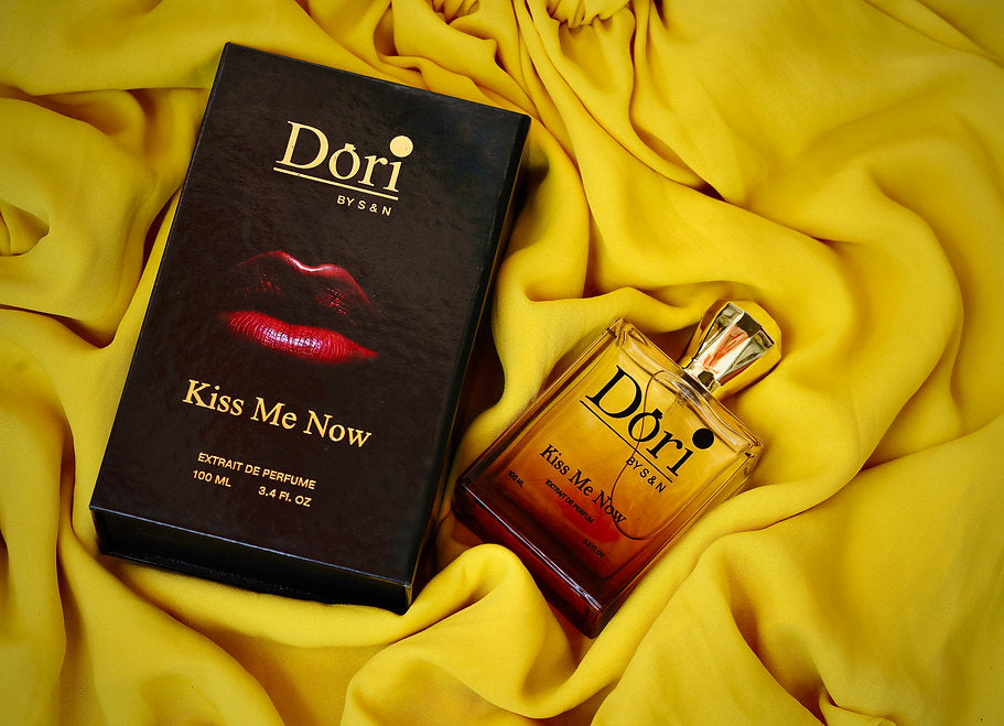 Kiss Me Now women perfume bottle with elegant packaging resting on a yellow fabric background