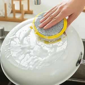 Hand using double-sided dishwashing sponge to clean white frying pan under kitchen faucet