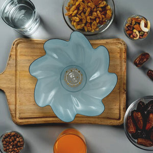 Flower shaped plastic fruit plate in blue on a wooden tray surrounded by various snacks and drinks