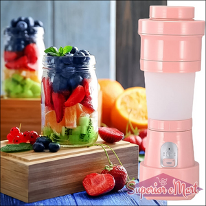 Pink foldable electric juicer blender with fresh fruit in jars on a wooden table