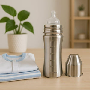 Superior eMart stainless steel baby milk bottle with measurement markings beside a folded baby onesie