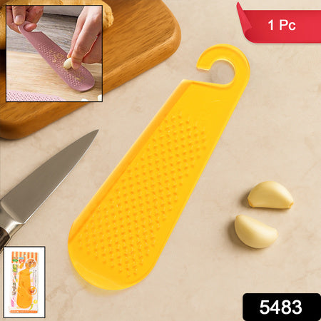 Yellow garlic and ginger grater tool on a countertop with garlic cloves and a knife