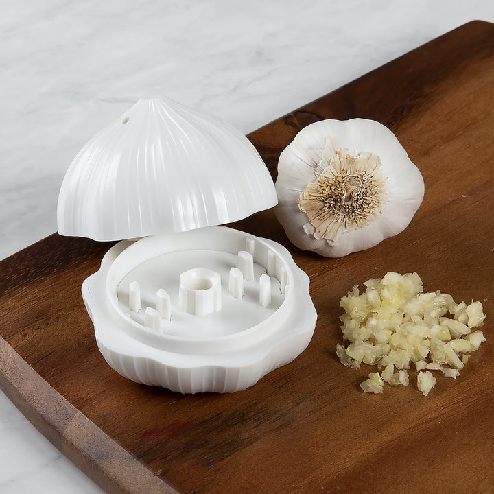 Garlic press sharpener in white with minced garlic next to it on a wooden cutting board
