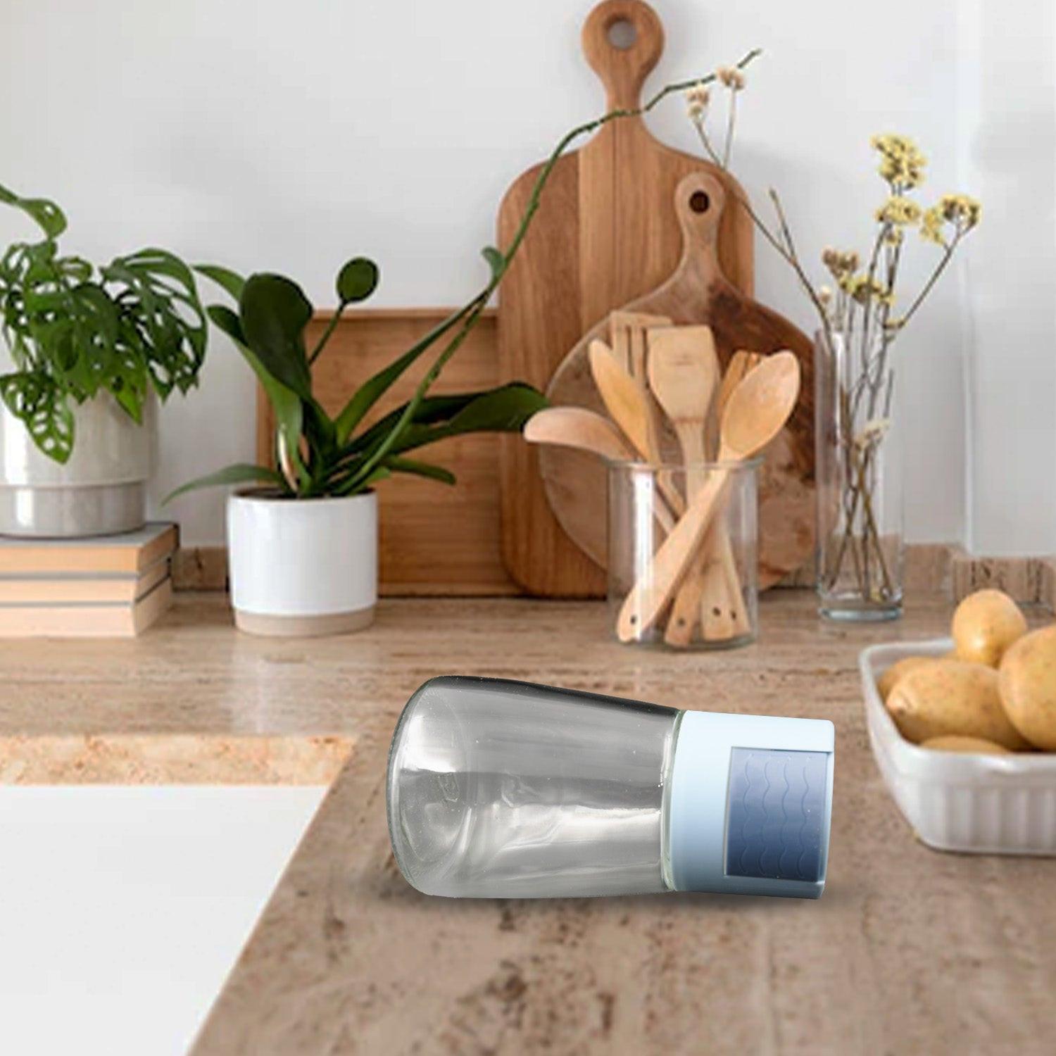 Stylish glass salt dispenser for cooking on a kitchen countertop with plants and utensils
