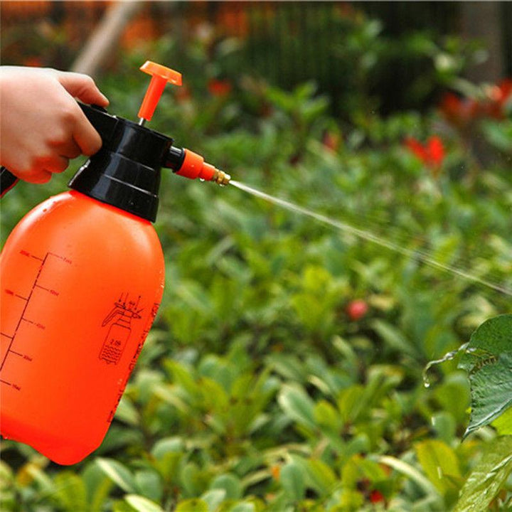 Hand-held garden sprayer in use, watering plants in a vibrant garden setting