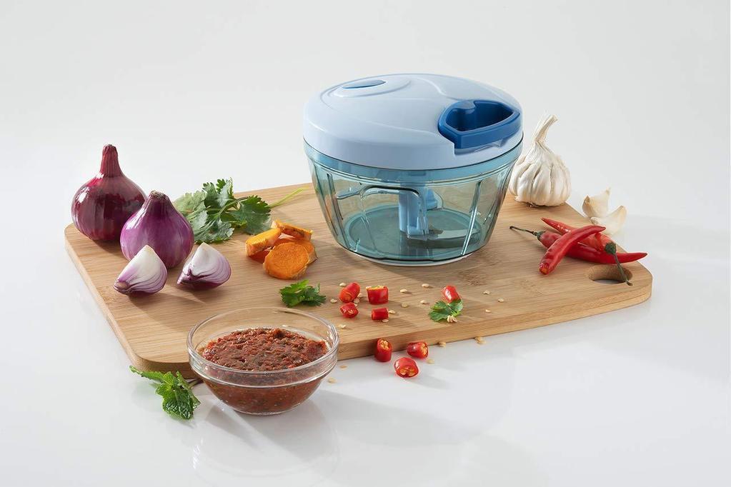 Handheld vegetable chopper in blue with chopped ingredients and spices on a wooden cutting board