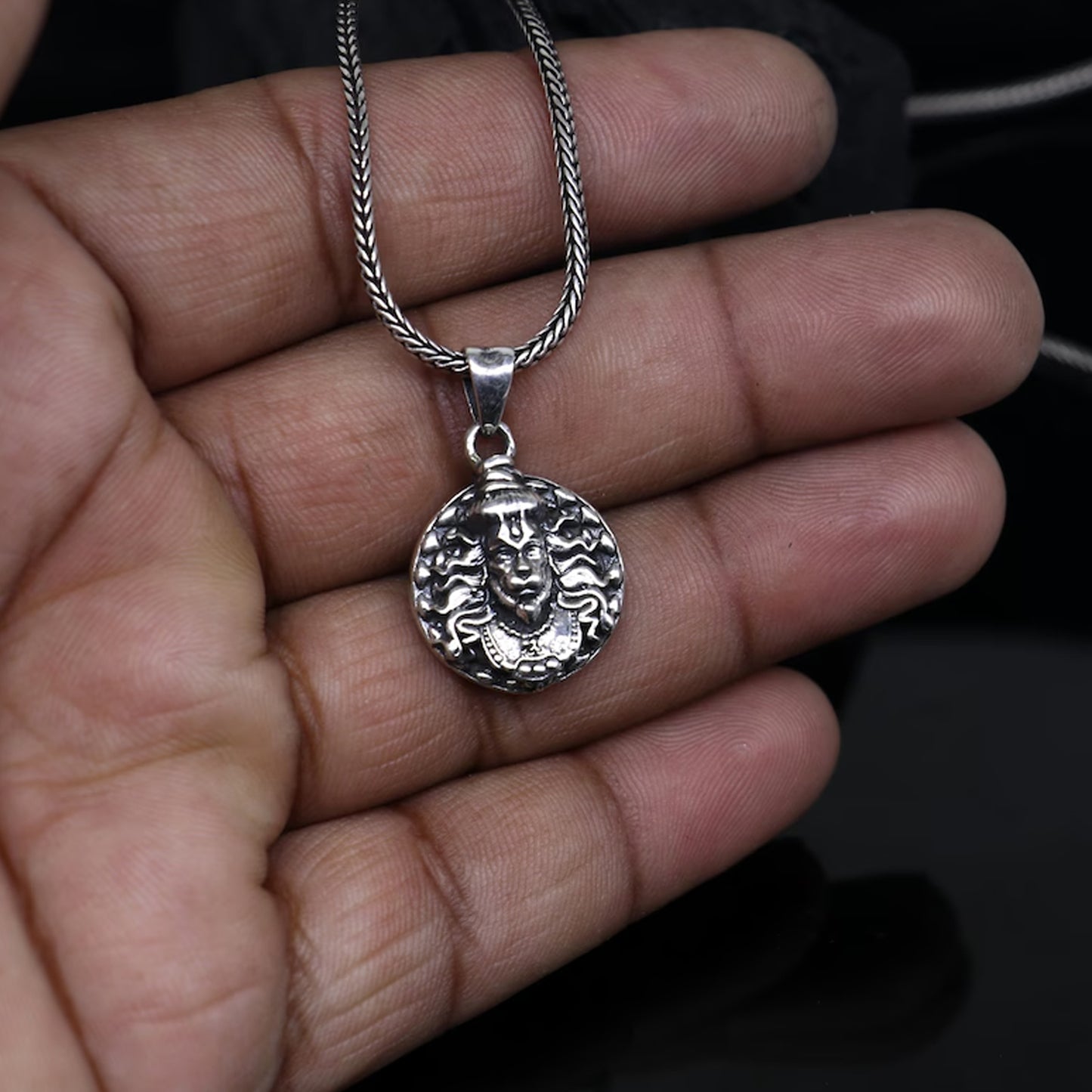 Hanuman facelocket necklace in silver with intricate detailing, held in a hand for scale