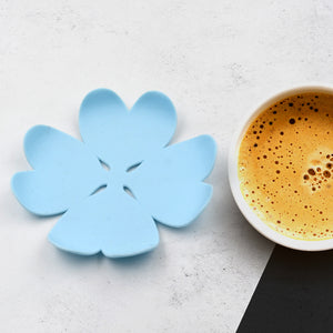 Blue flower-shaped heat resistant coasters set next to a cup of coffee