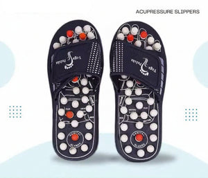 A pair of dark navy blue acupressure slippers with white and red massage nodes, displayed against a light blue and white background with promotional text overlays.