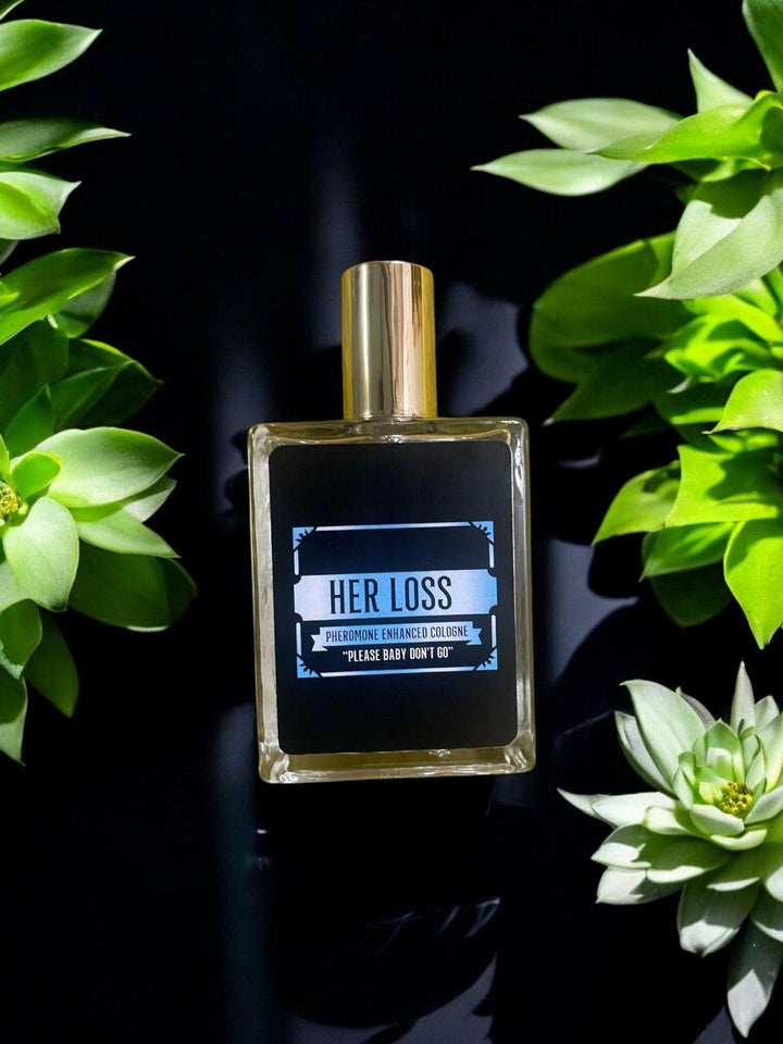 Her Loss signature perfume in a sleek bottle, presented on a dark surface with green succulent plants.