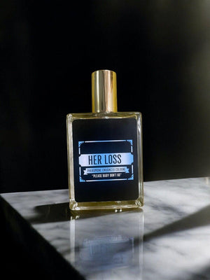 Her Loss signature perfume displayed on a marble surface, featuring a gold cap and sleek design.