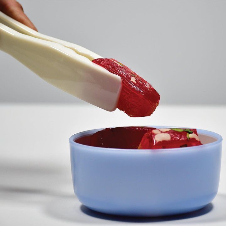 Kitchen bread tongs lifting jelly from a blue bowl for easy serving and handling