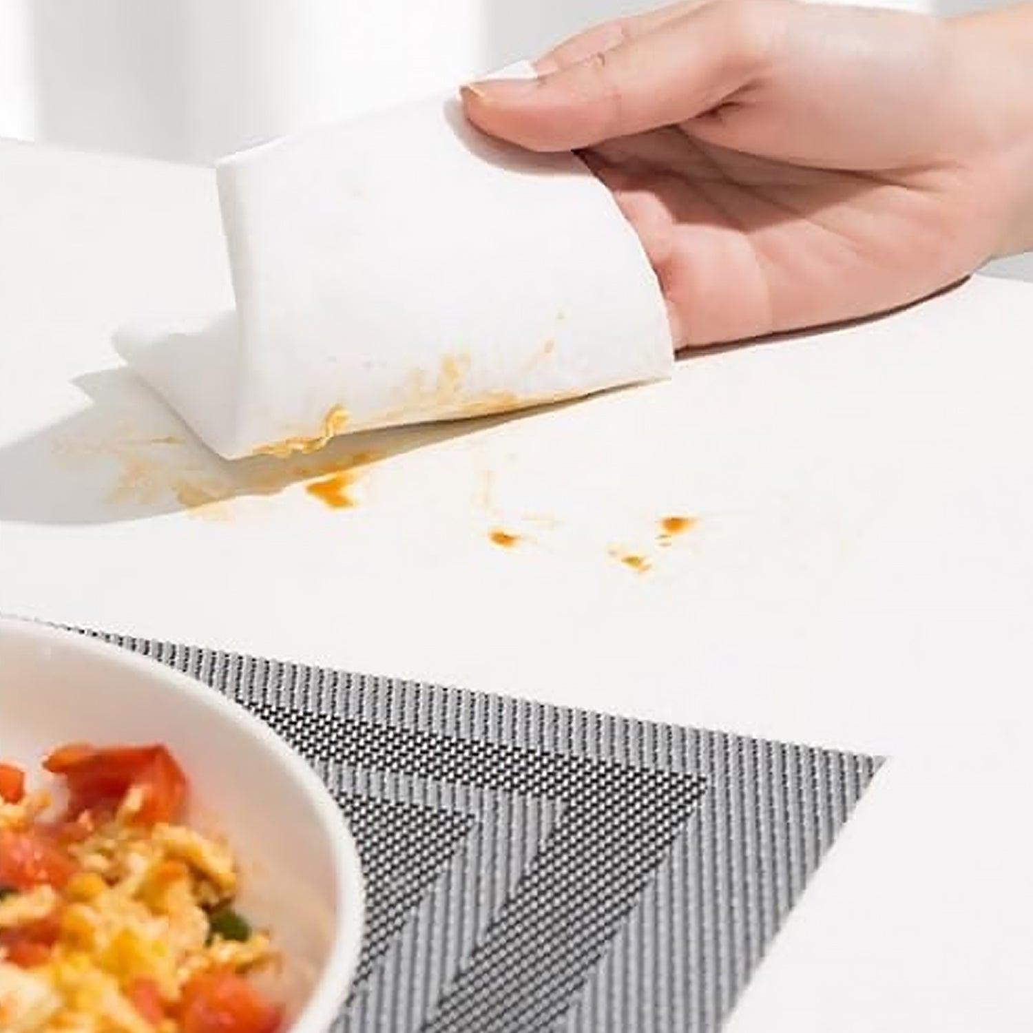 Hand using kitchen cleaning wipes to remove food stains from a tabletop surface