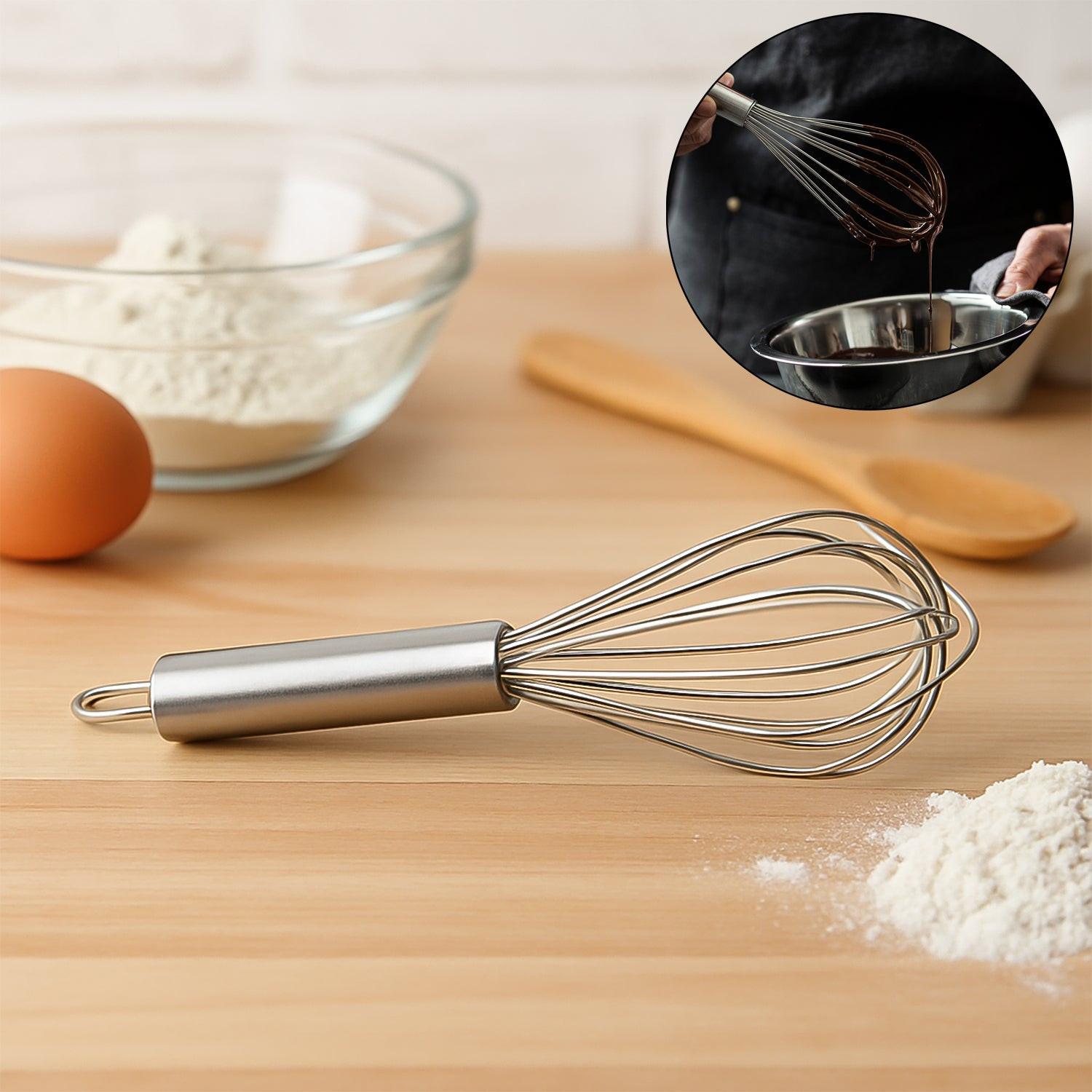 Small stainless steel balloon whisk on a wooden countertop with baking ingredients for easy mixing